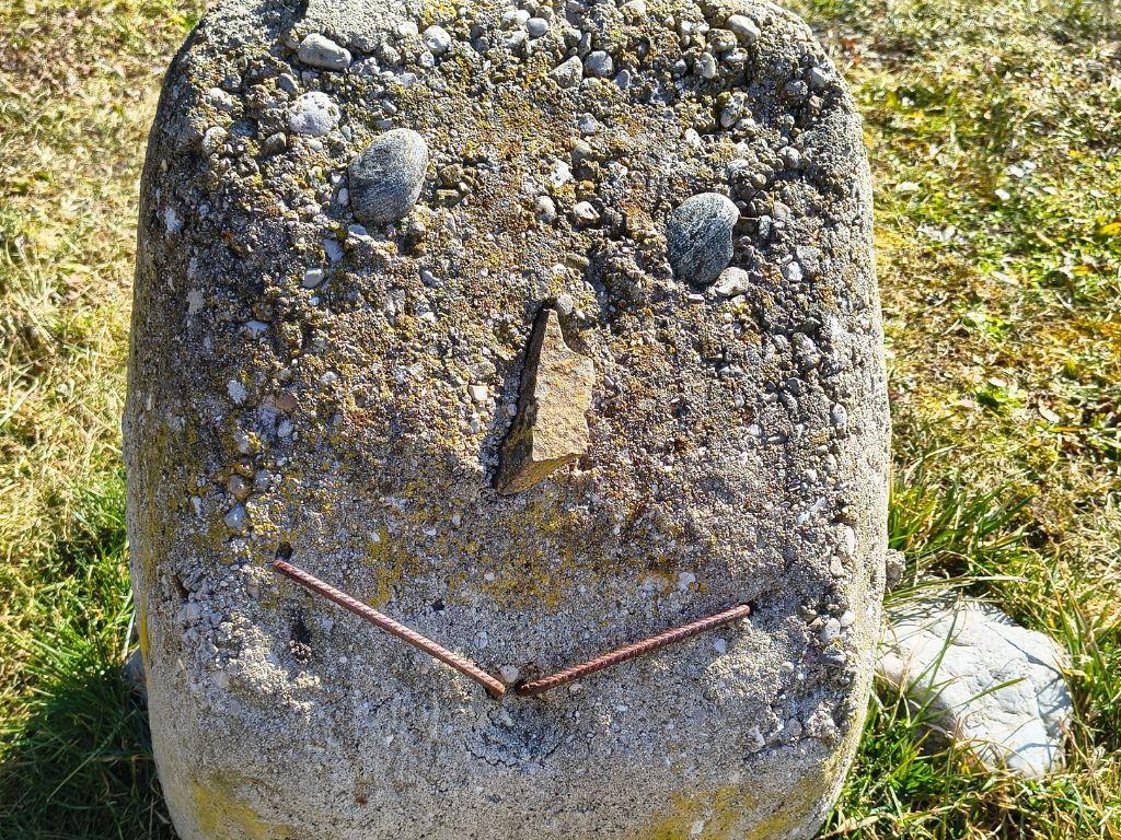 Großer Stein mit 2 Kieselsteinen als Augen, einem eckigen Stein als Nase und 2 Metallklammern bilden einen lachenden Mund.