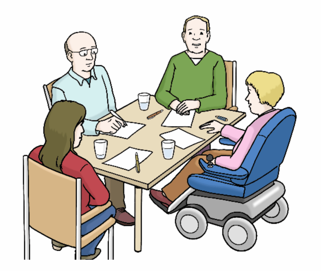 eichte Sprache Bild einer Prüfgruppe. 4 Personen sitzen am Tisch. Es sind 2 Frauen und 2 Männer. Eine Frau sitzt in einem elektronischen Rollstuhl. Auf dem Tisch liegen Papier und Stifte.