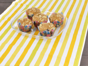 Beerenmuffins in einer Glasschüssel auf einer gelbgestreiften Tischdecke.